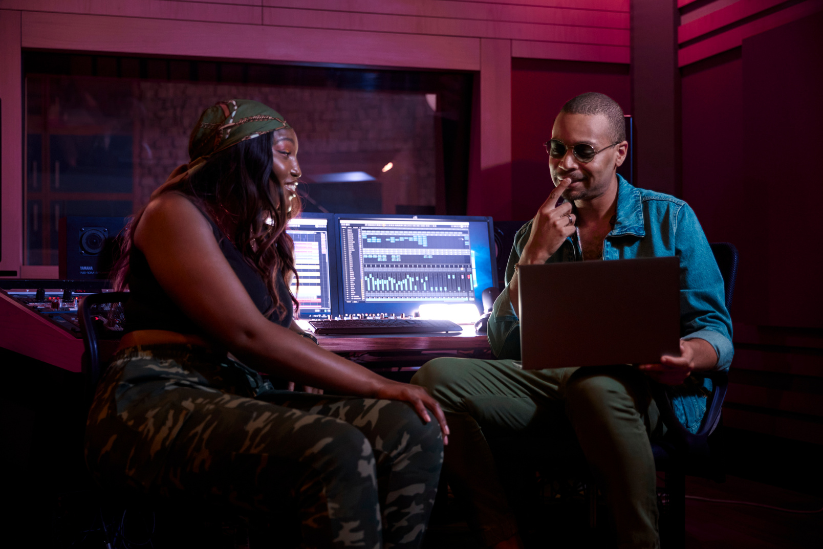 African-american female artist working with male music producer on laptop in music studio